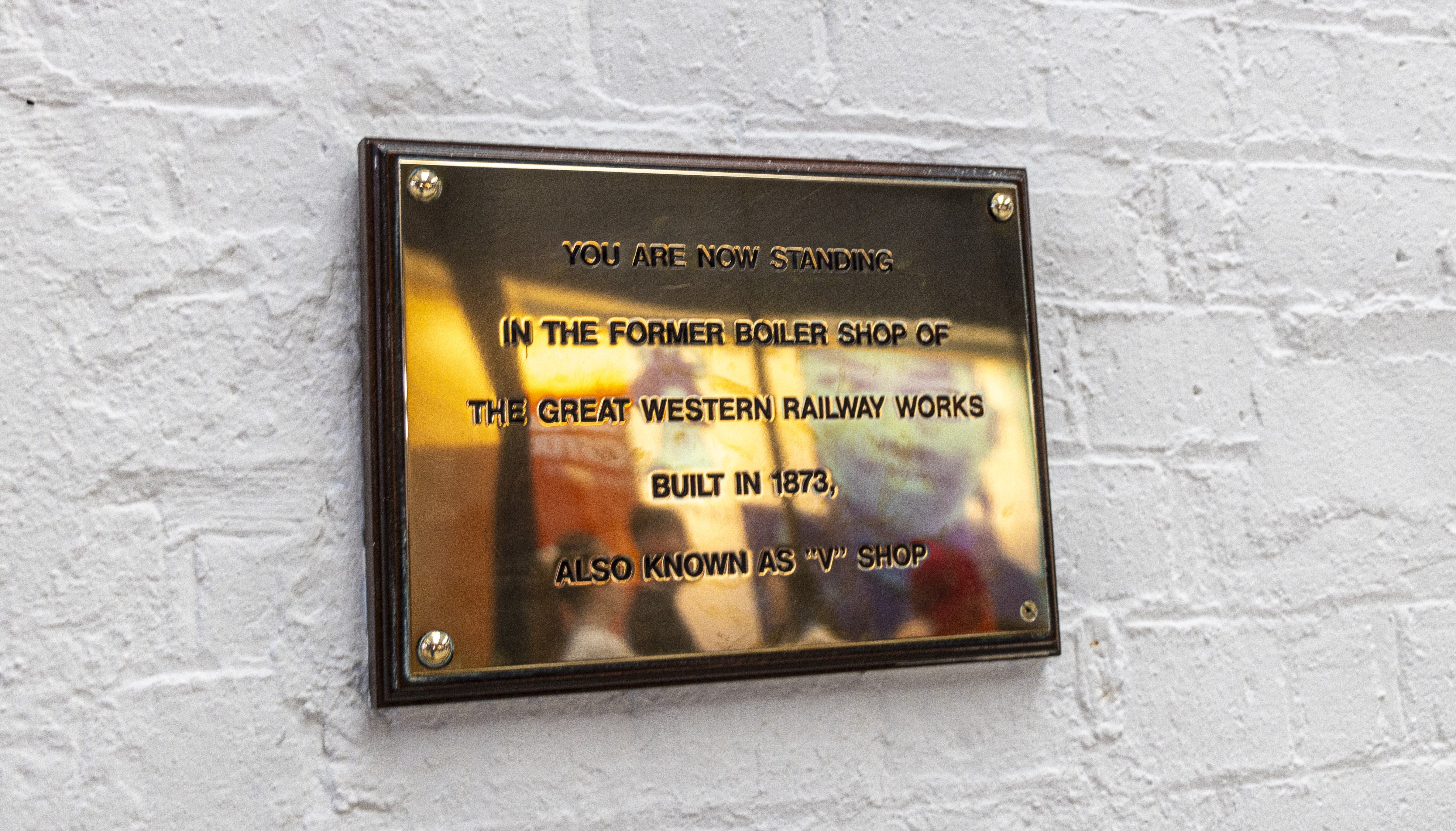 A golden plaque on the wall reads, You are now standing in the former boiler shop of the Great Western Railworks built in 1873